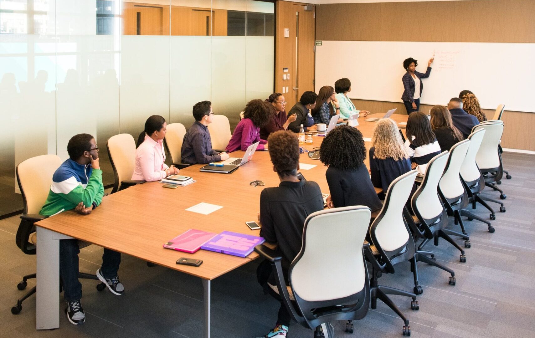 Various adults in a collaborative boardroom meeting with a presentation in progress.